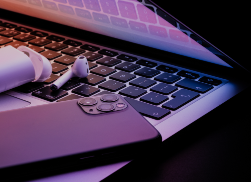 An open laptop with a smartphone and wireless headphones sitting on the keyboard